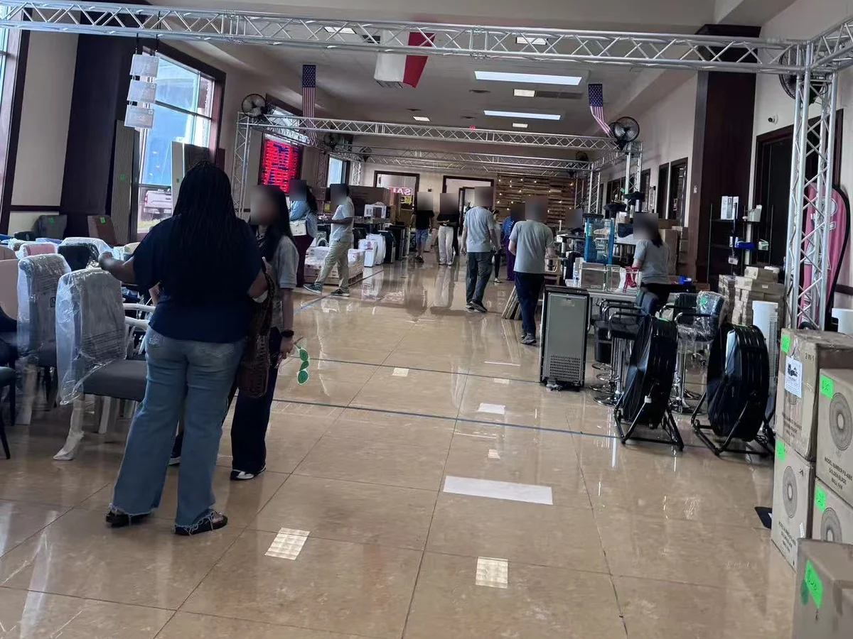 Buyers along the main aisle of the Cube-Age Houston sale floor among the fans and small appliances