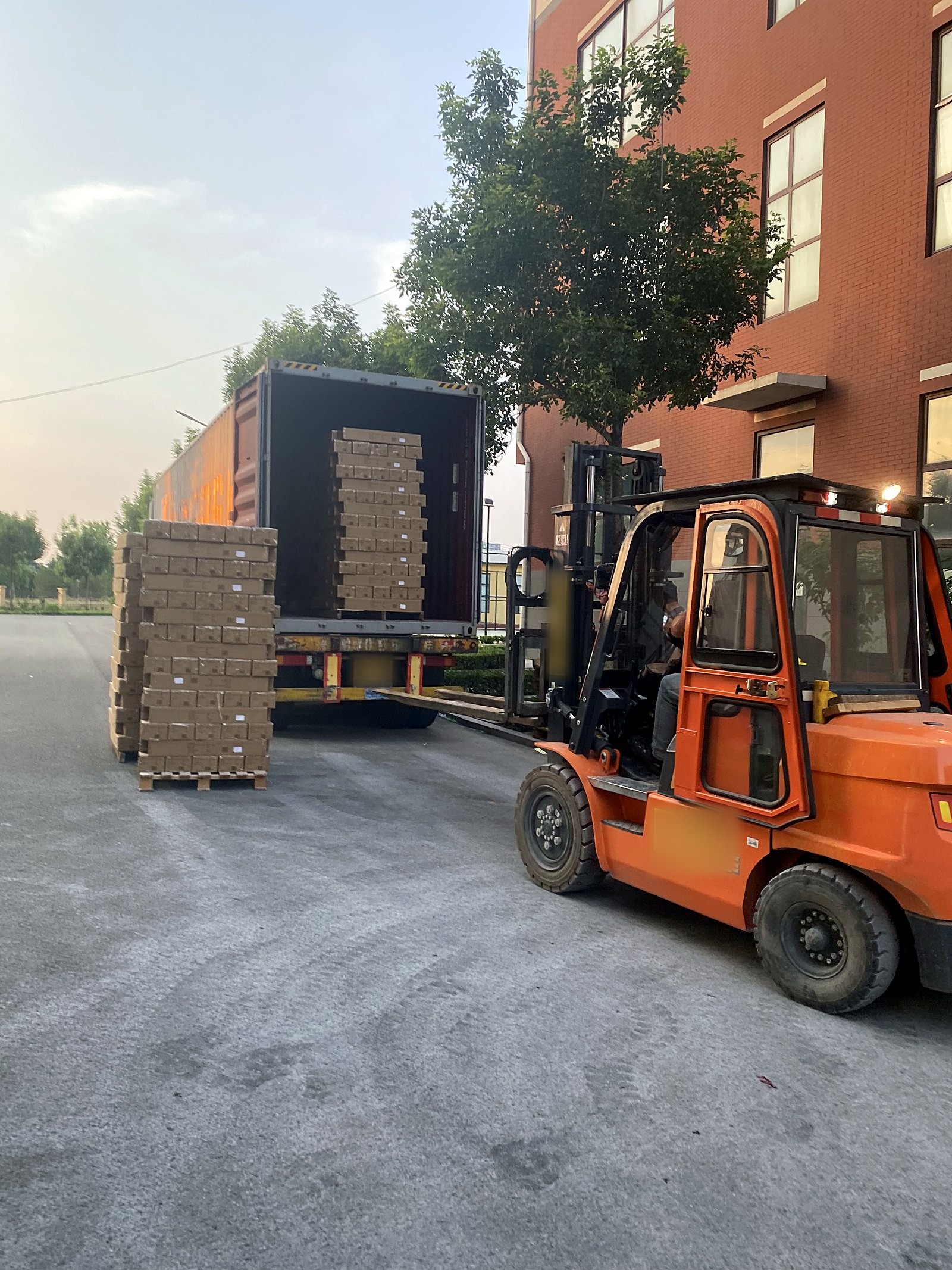 A forklift loading cartons of kites into a container truck at the factory gate