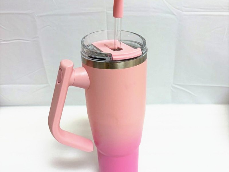 A peach-pink insulated tumbler with a handle, lid and straw