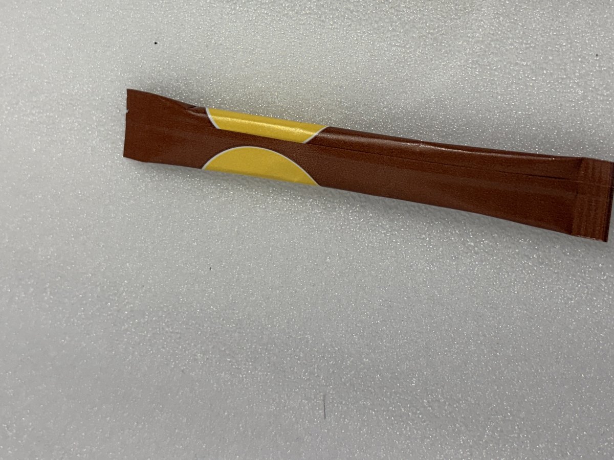 A single-serve stick of brown cane sugar lying on a pale background