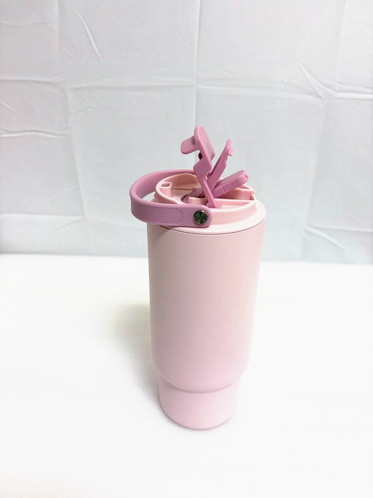 A pink insulated travel cup with a flip-up straw lid and a carry loop