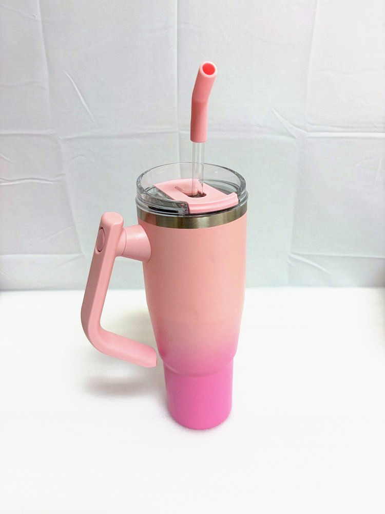 A peach-pink stainless steel tumbler with a carry handle, clear lid and colored straw